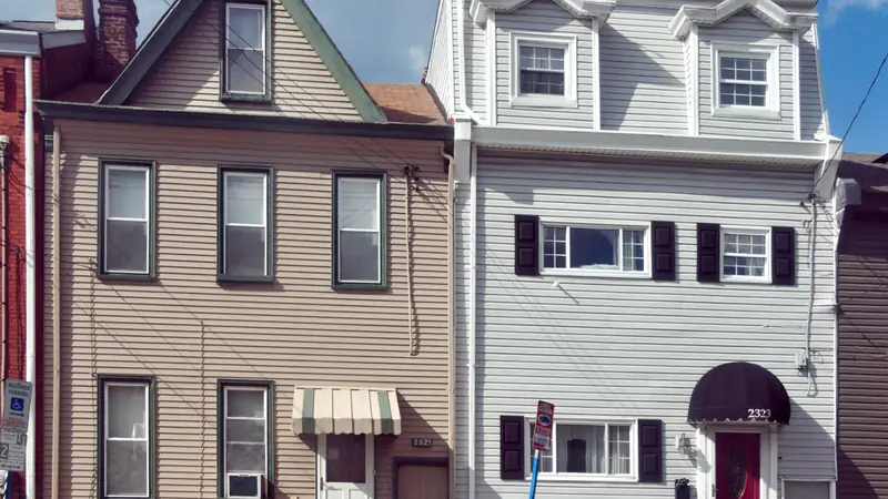 Two attached older houses, one with tan siding and one with white siding